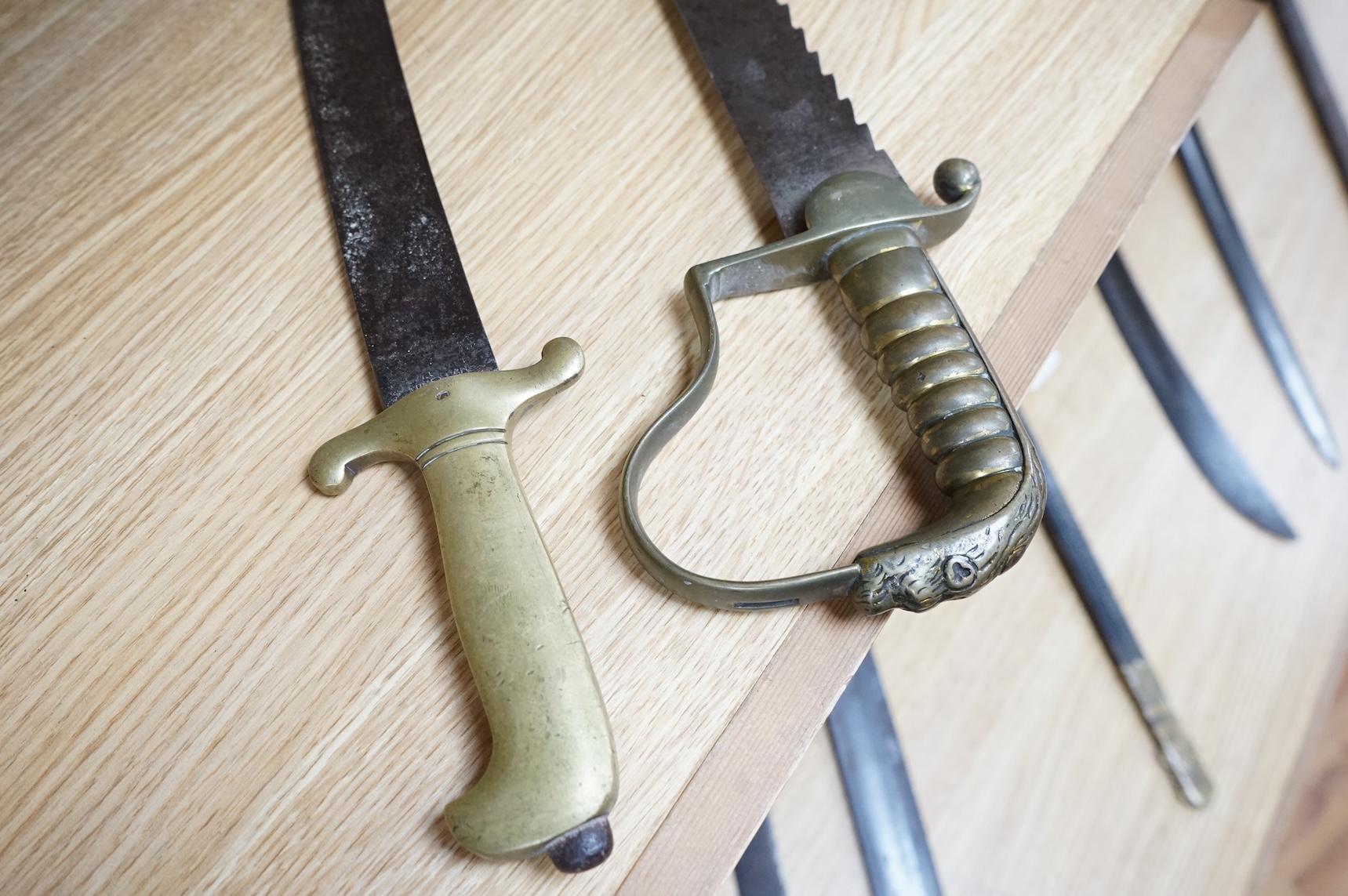 A British Pioneer’s sidearm with brass stirrup hilt, lion’s head pommel and sawback blade, together with an Imperial German sidearm with one piece brass hilt and slightly curved single edge blade